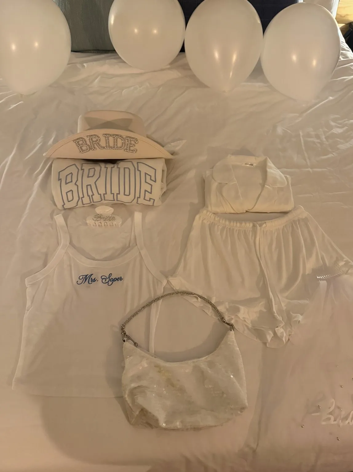 Flat-lay of a bride hat, sweatshirt, tank, pyjamas and sequin bag